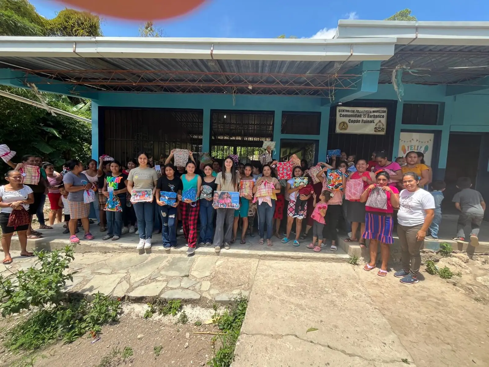 Un grupo numeroso de mujeres, niñas y niños con sus kits frente al Centro de Educación Básica Francisco Morazán, en El Barbasco, Copán Ruinas, junto al equipo de Days for Girls in Honduras.